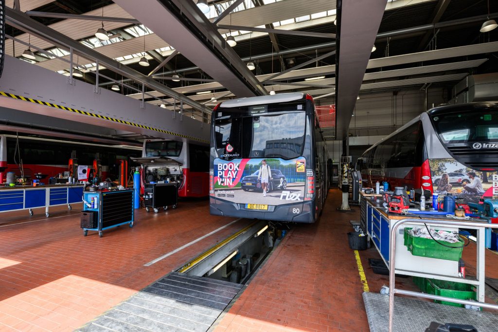 Foto der Reparatur- und Wartungswerkstatt des Busdienstes der CFL. Vier Busse sind von hinten zu sehen. Ein Elektrobus ist zu erkennen und steht derzeit auf der Reparaturbrücke der Werkstatt.